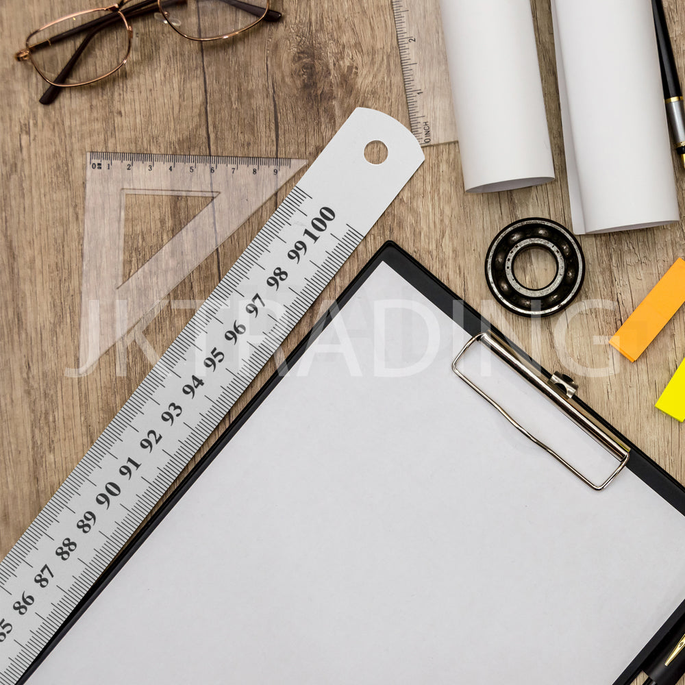 Stainless steel ruler resting diagonally across a silver aluminum office clipboard next to a roll of paper.
