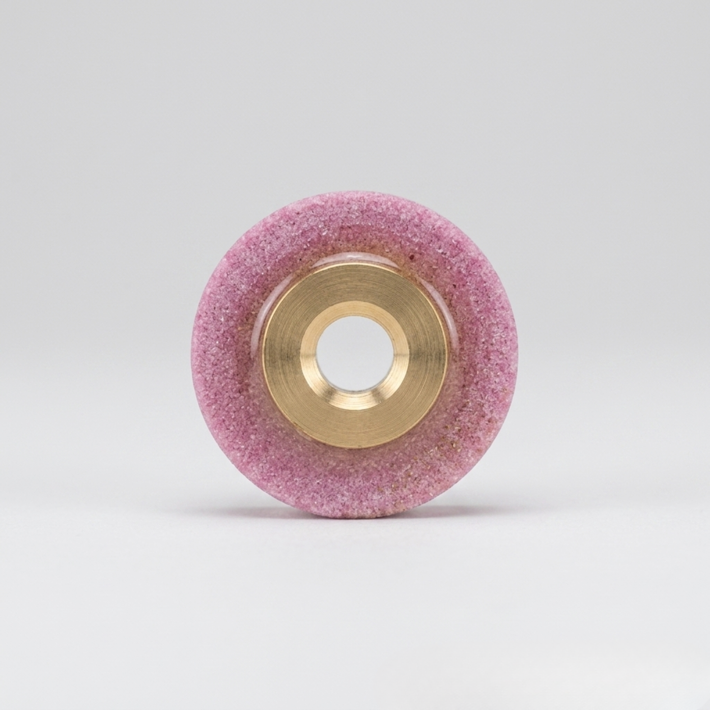 a professional pink whetstone blade sharpener with a brass center hub, designed for industrial rotary fabric cutters, isolated on a seamless white background.