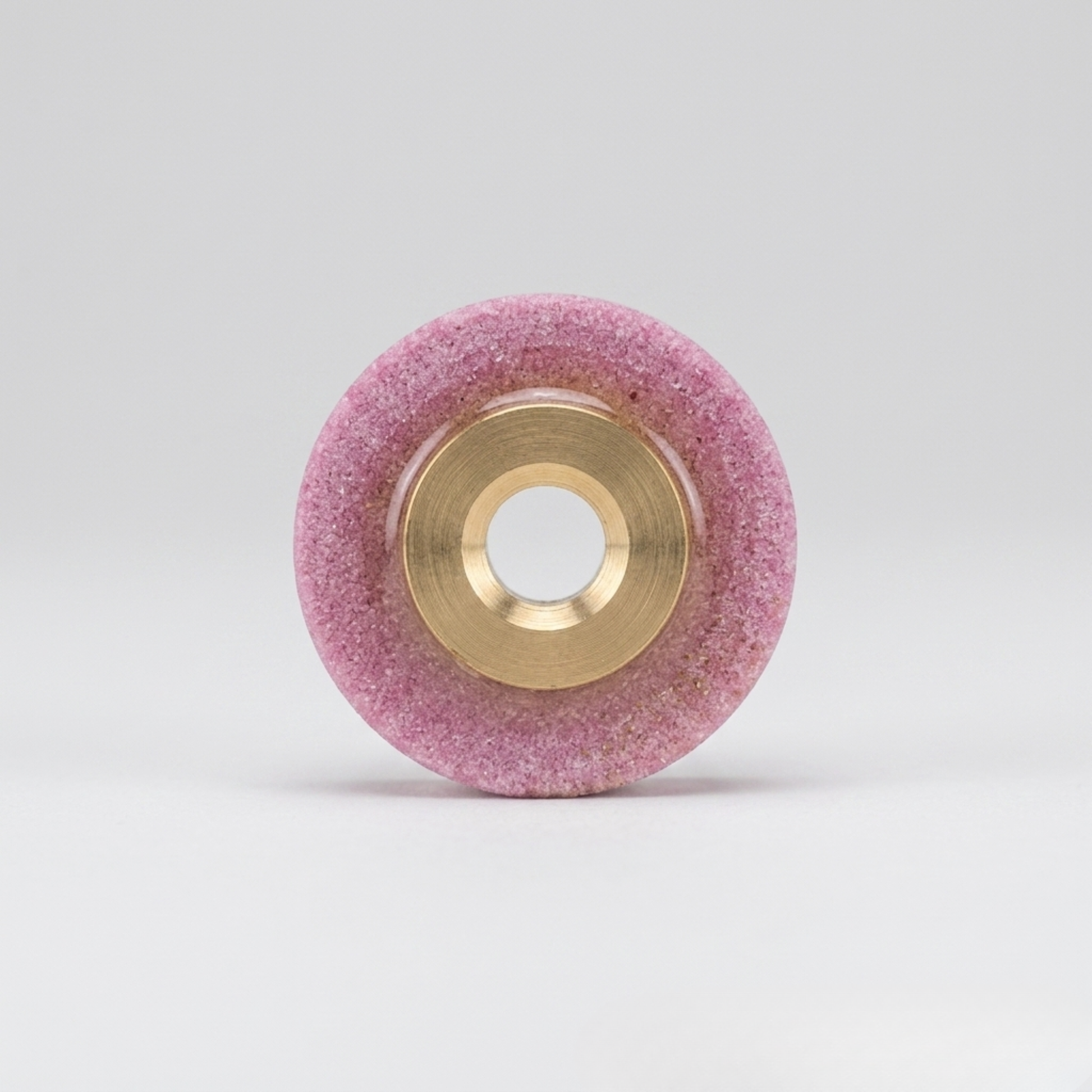 a professional pink whetstone blade sharpener with a brass center hub, designed for industrial rotary fabric cutters, isolated on a seamless white background.