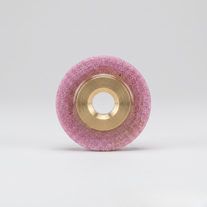 a professional pink whetstone blade sharpener with a brass center hub, designed for industrial rotary fabric cutters, isolated on a seamless white background.