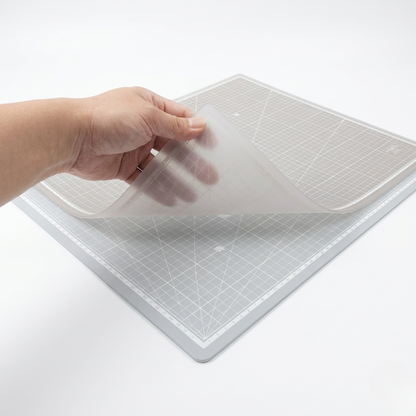 Hand lifting a flexible translucent self-healing cutting mat to showcase its semi-transparent plastic material properties.