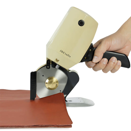 Hand operating a heavy-duty industrial electric fabric cutter to slice cleanly through a sheet of thick brown leather.