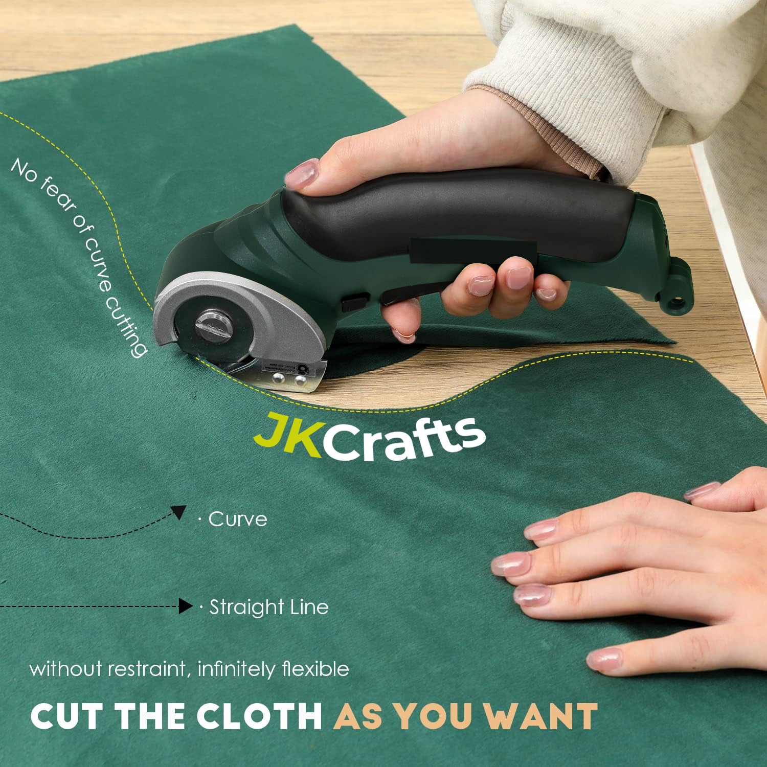 Crafter cutting a smooth curve along a patterned line into green cotton cloth material using cordless scissors.