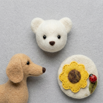 Miniature wool felted crafts including a white bear head, a brown dog head, and a yellow sunflower design.