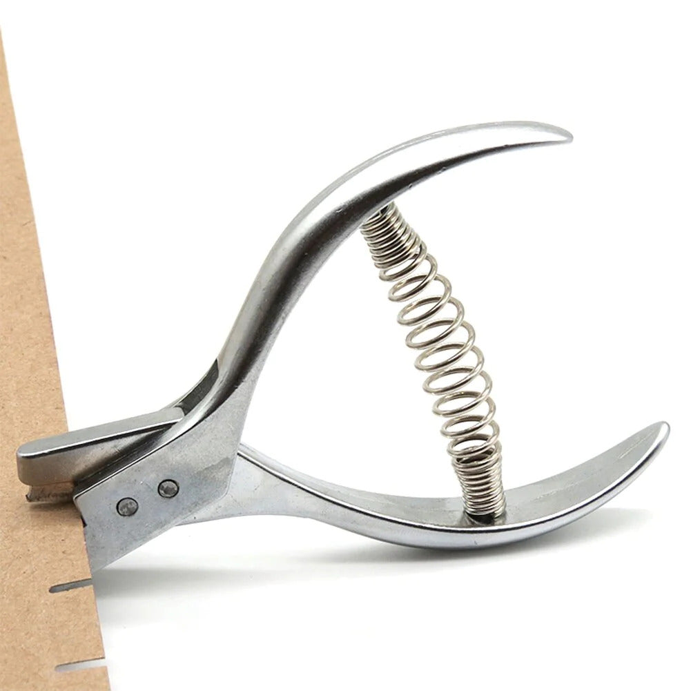 Metal pattern notcher pliers resting flat on a white cardstock sheet showcasing its precision alignment slot.