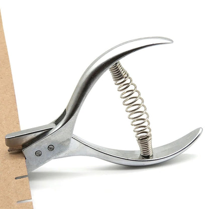 Metal pattern notcher pliers resting flat on a white cardstock sheet showcasing its precision alignment slot.