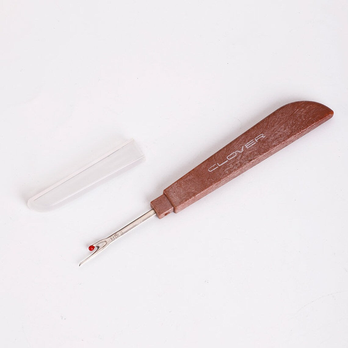 Ergonomic wooden handle sewing ripper laid flat next to its clear plastic protective safety cap.