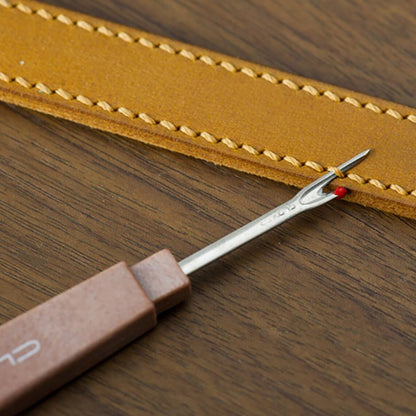 Sharp steel stitch unpick tool positioned against a heavy-duty stitched tan leather belt strap.