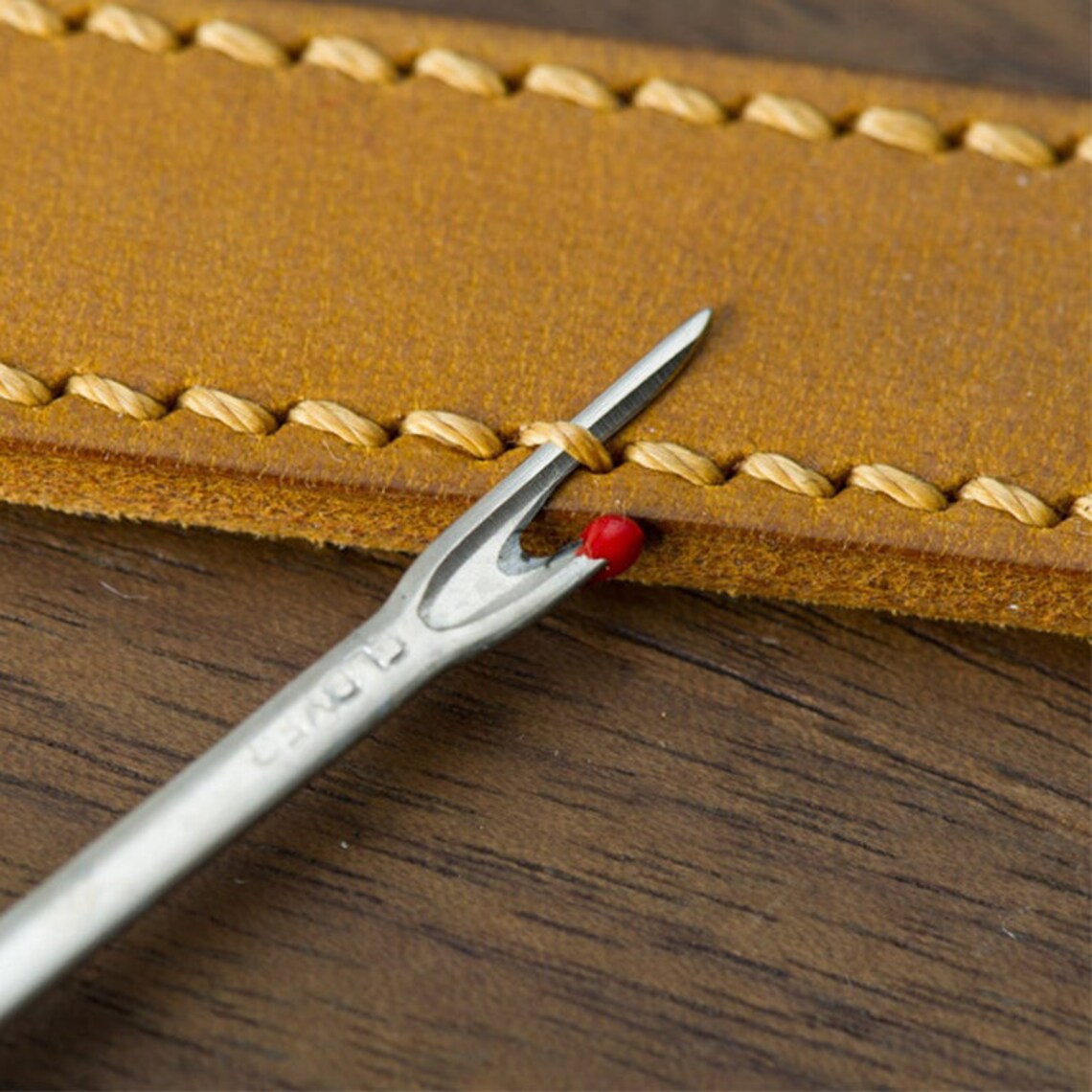 Close-up view of the fine-tipped metal blade sliding under a durable thread loop to slice a leather seam open.
