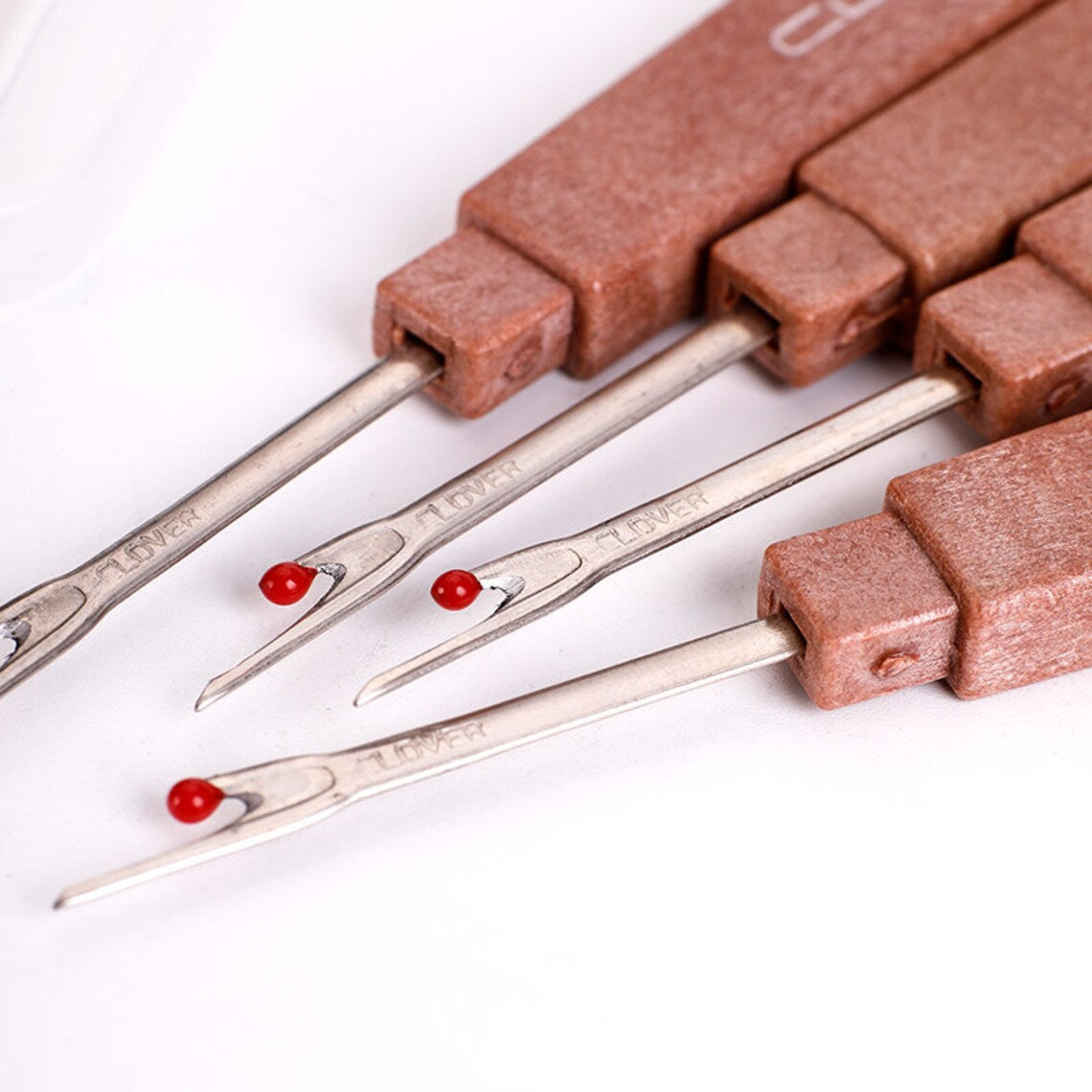 Close-up compilation layout showcasing the sharp curved cutting edges and red safety ball tips of three seam rippers.