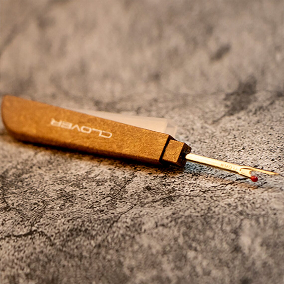 Premium wood-grain tailored embroidery thread slasher tool resting horizontally on a rustic stone workspace surface.