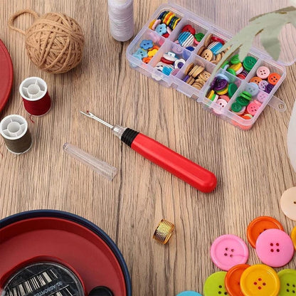 Red lighted stitch picker resting on a wooden crafting table surrounded by plastic sorting boxes and multi-colored buttons.