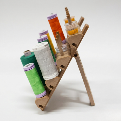 Side profile view of a wooden sewing spool organizer showing its angled display and rear support leg configuration.