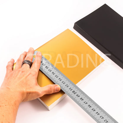 Designer using a long metal ruler to align and mark layout grids onto a yellow hardcover sketchbook journal.