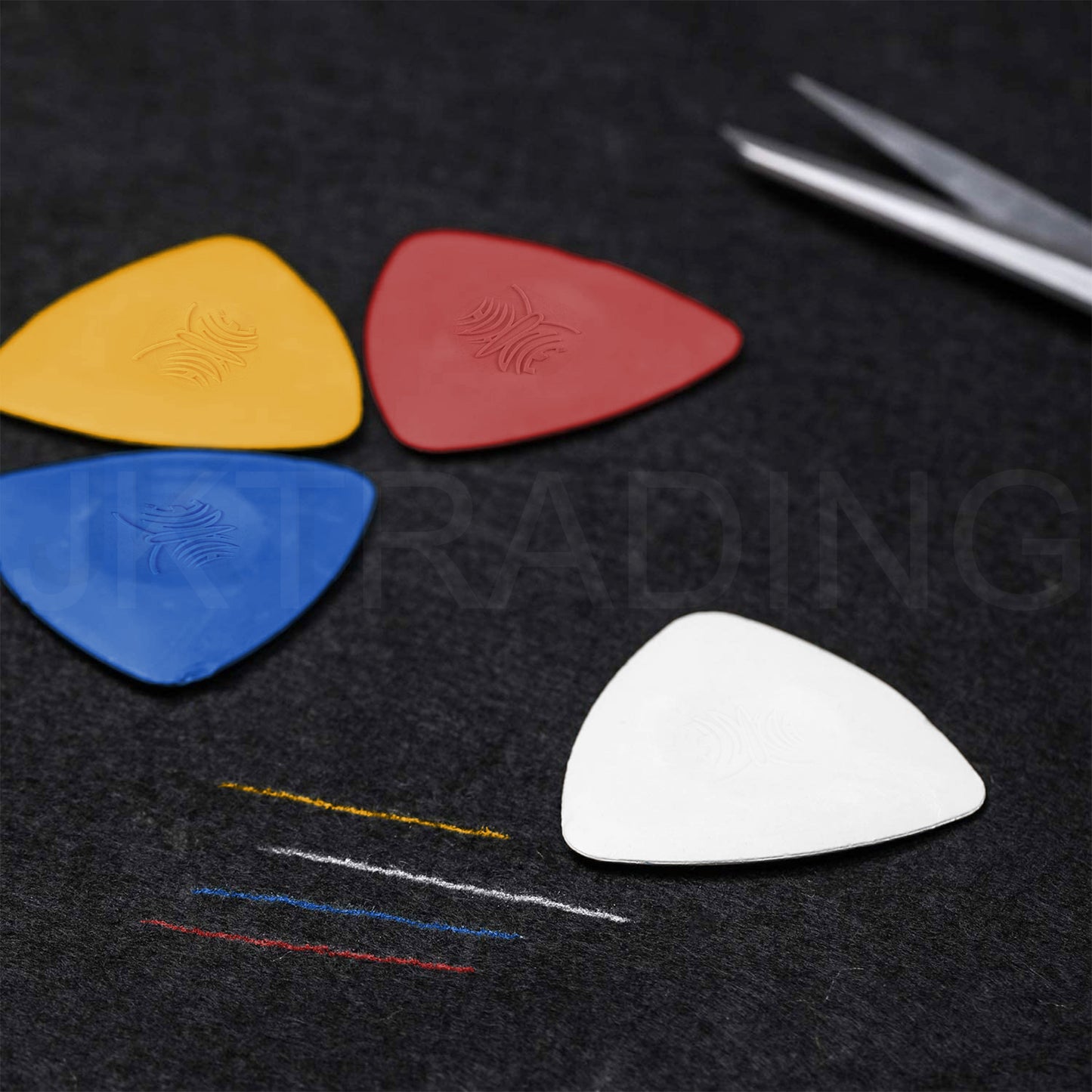 Yellow, red, and white fabric marking crayons resting on textured dark cloth next to sewing needles and scissors.