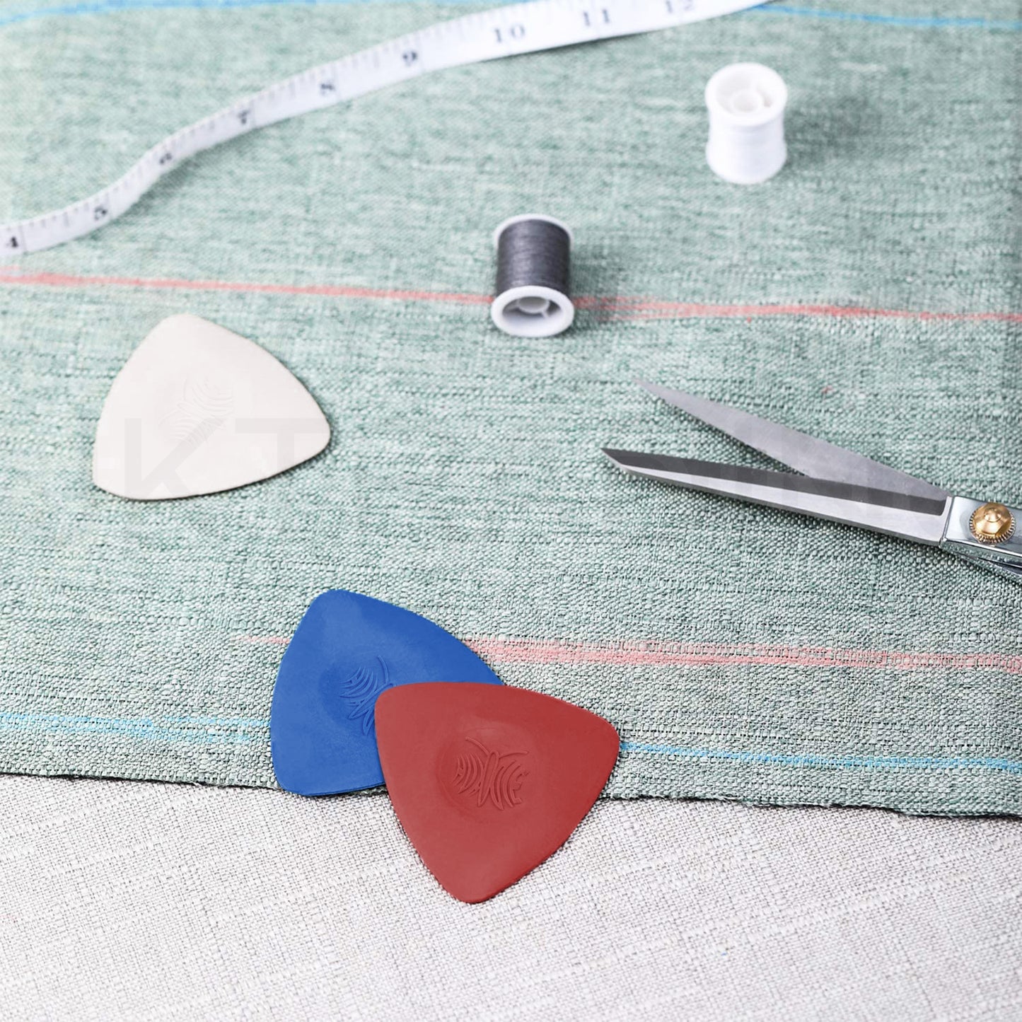 Three triangular sewing chalk pieces placed on a light green linen workspace beside a tape measure and thread spool.