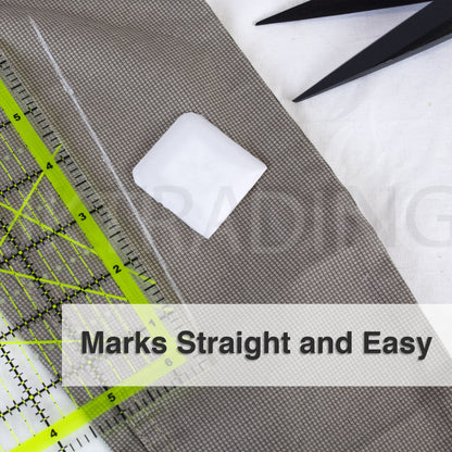 Square white tailors wax marker drafting smooth, straight lines on khaki garment fabric using a clear grid ruler.