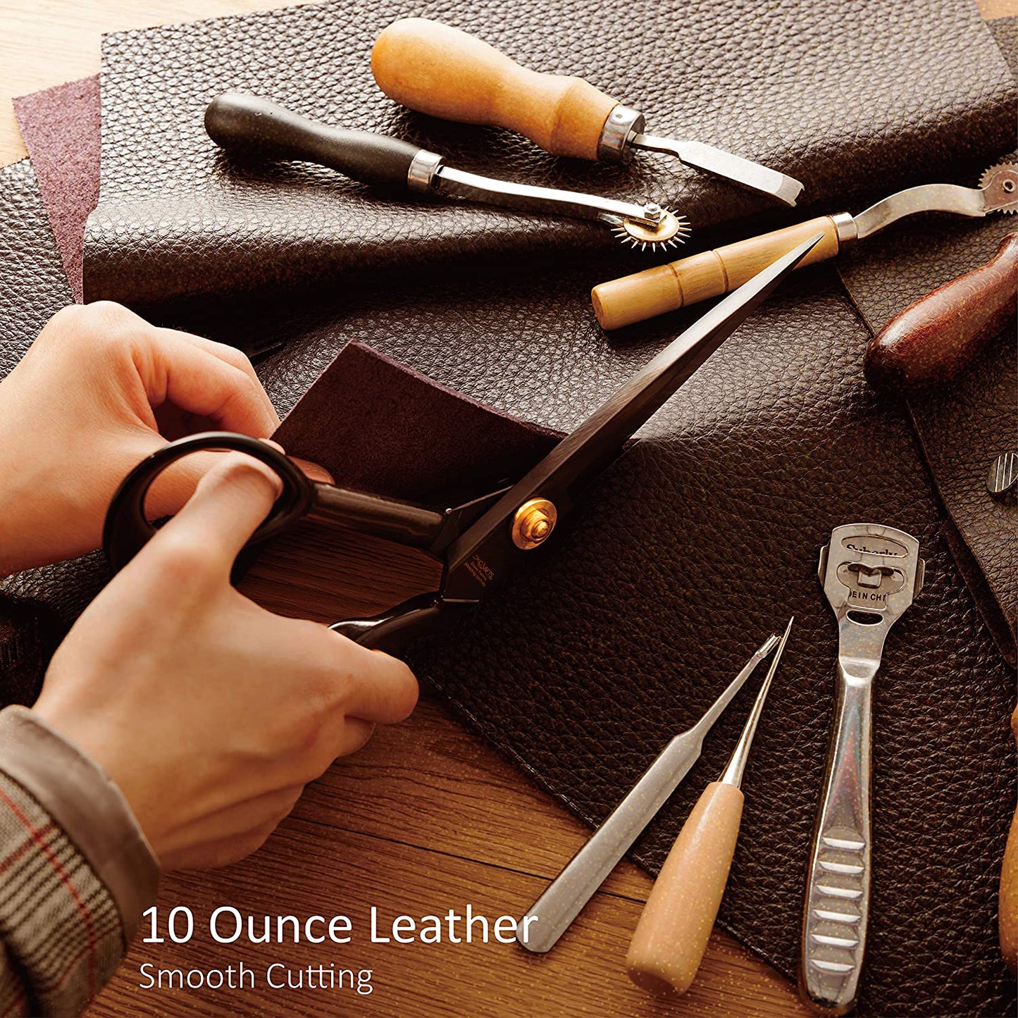 Leatherworking tools on a leather surface with a hand holding scissors.