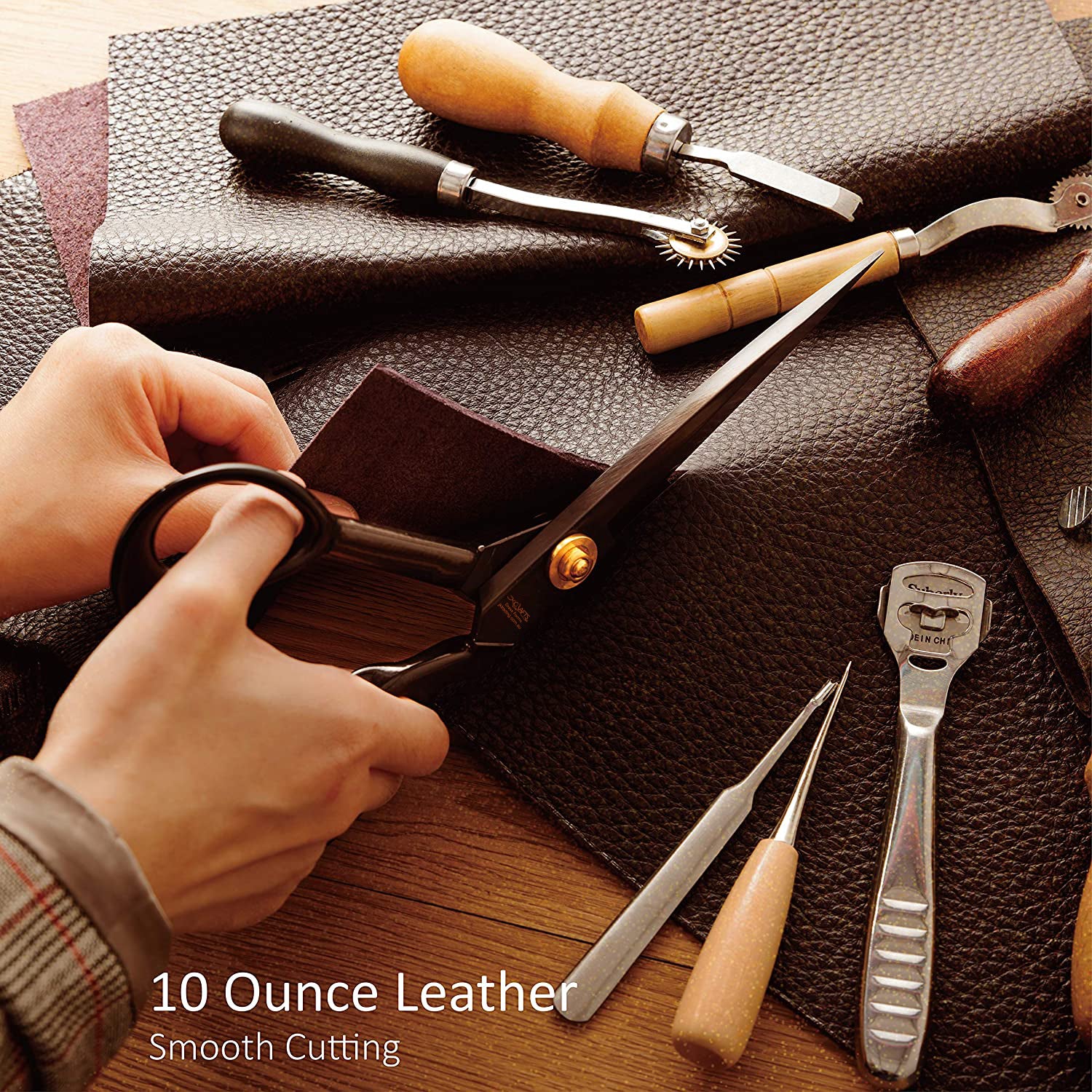 Leatherworking tools on a leather surface with a hand holding scissors.