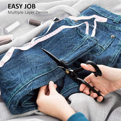 Person cutting multiple layers of denim fabric with scissors on a gray surface.