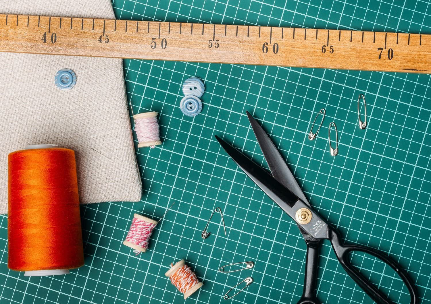 Sewing tools including scissors, thread, and a ruler on a green cutting mat.