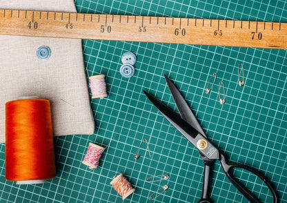 Sewing tools including scissors, thread, and a ruler on a green cutting mat.