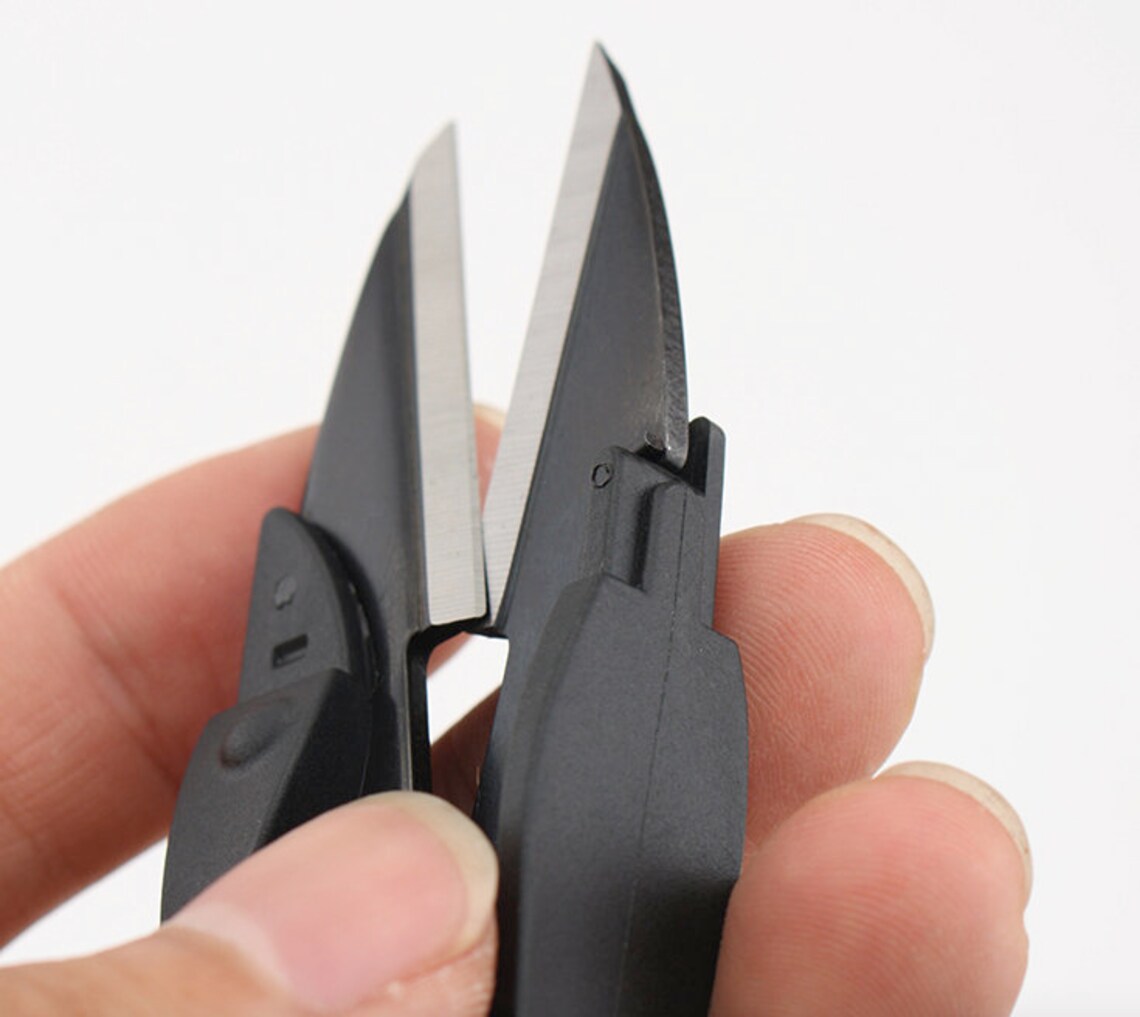 Hand squeezing the non-slip safety handle of the black thread trimmer to demonstrate precise cutting blade alignment.